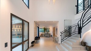 A spacious hallway with a staircase, a seating area with sofas, and a large window. - Villa Blue Pearl, 10 pers, piscine chauffée, 10 minutes plage à pieds (SAINTE LUCIE DE PORTO VECCHIO)