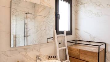 A modern bathroom with a marble wall, a large mirror, a wooden vanity, and a ladder.
