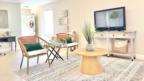 A living room with wicker chairs, a round coffee table, a television on a cabinet, and artwork on the walls. - Contemporary 4-Bed Home Steps from Downtown & ATT Center (San Antonio)