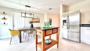 A modern kitchen with a stainless steel refrigerator, a wooden island with drawers, and a dining area with chairs and a table. - Contemporary 4-Bed Home Steps from Downtown & ATT Center (San Antonio)