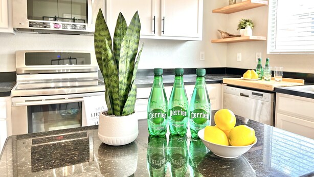 A kitchen with white cabinets, a stainless steel oven, a potted plant, Perrier water bottles, and a bowl of lemons. - Contemporary 4-Bed Home Steps from Downtown & ATT Center (San Antonio)