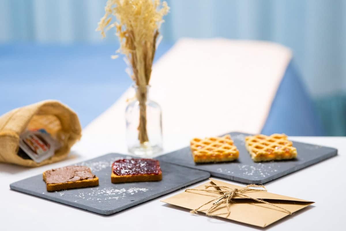 Una mesa con tres waffles cuadrados, un pastel pequeño cuadrado, una botella de vidrio y un saco de arpillera.