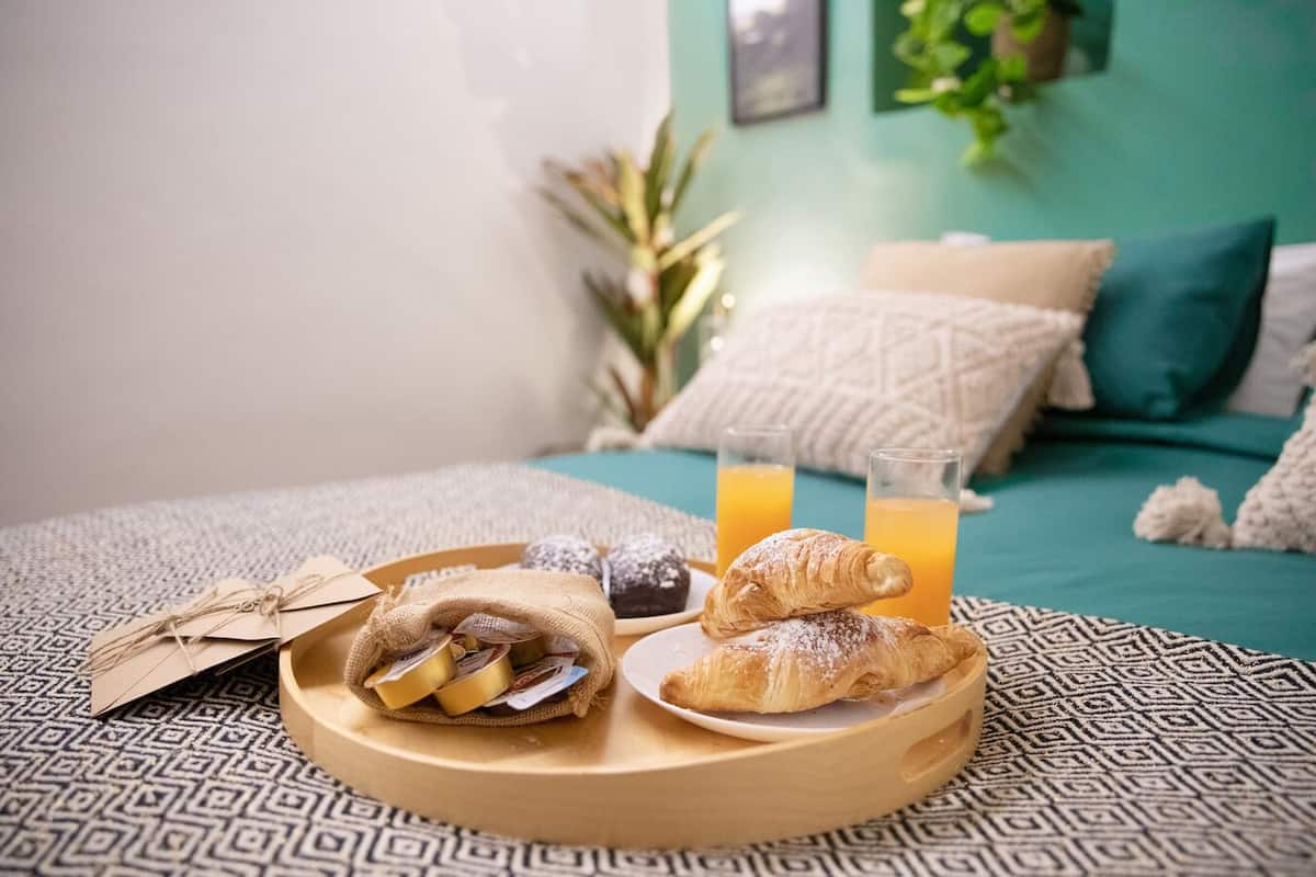 Un desayuno con bollos y zumo de naranja sobre una cama con ropa de cama estampada.