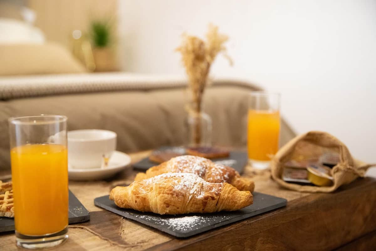 Un desayuno con un croissant, un vaso de jugo de naranja, una taza y una cesta sobre una mesa de madera.