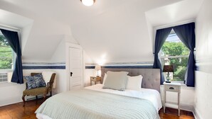 Ein Schlafzimmer mit einem großen Bett, einem Sessel, einem Nachttisch und einem Fenster mit Vorhängen.