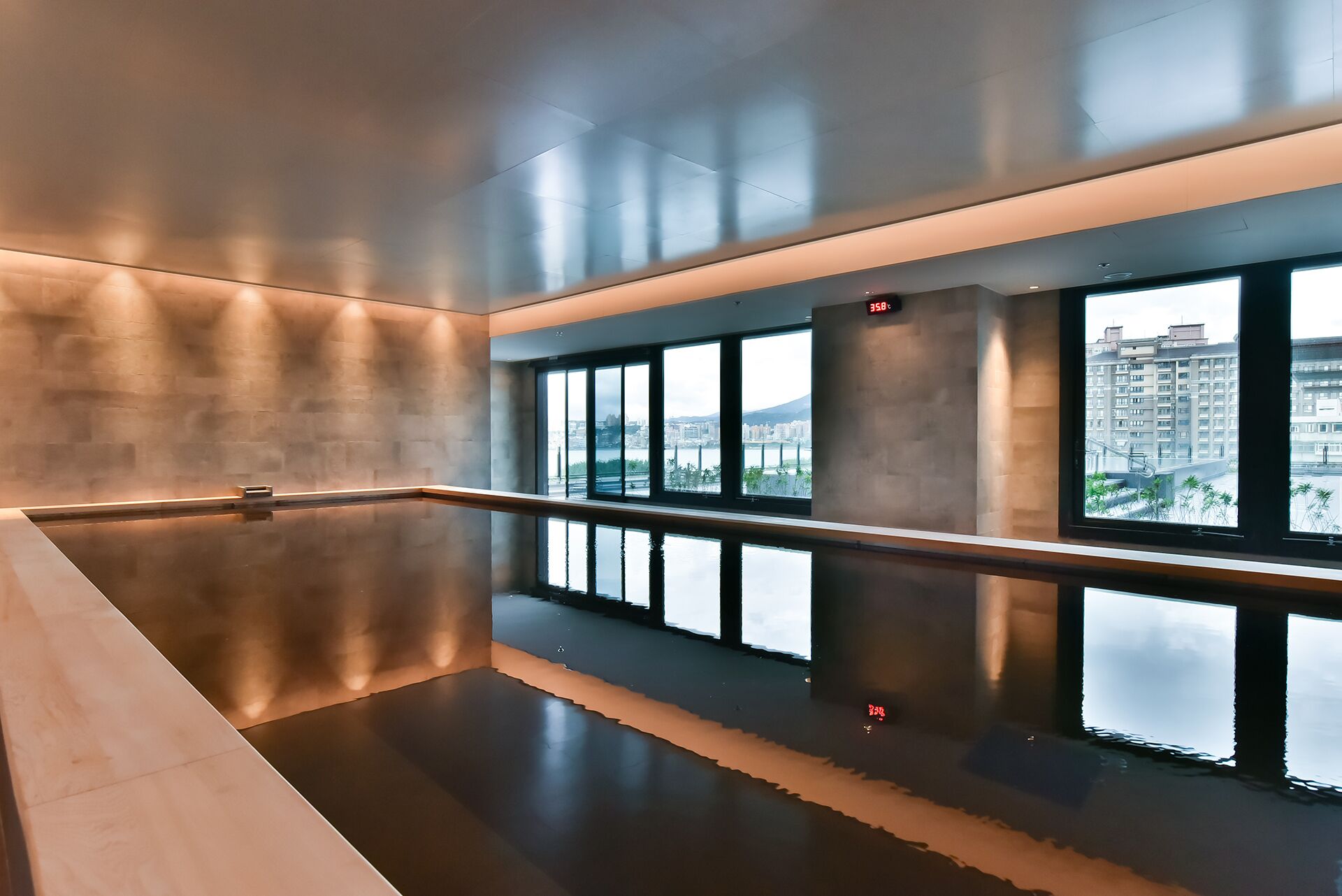 A modern indoor pool with a reflective floor, large windows offering a city view, and a minimalist design.