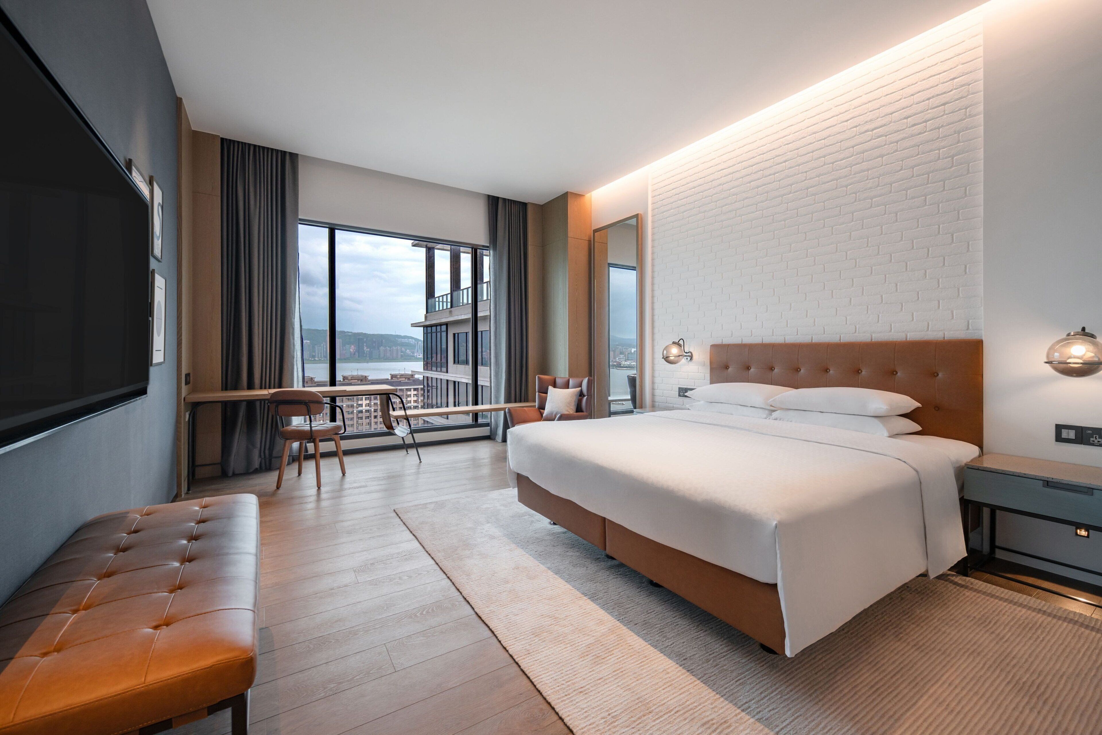 A modern hotel room with a large bed, a desk, and a balcony with a view.