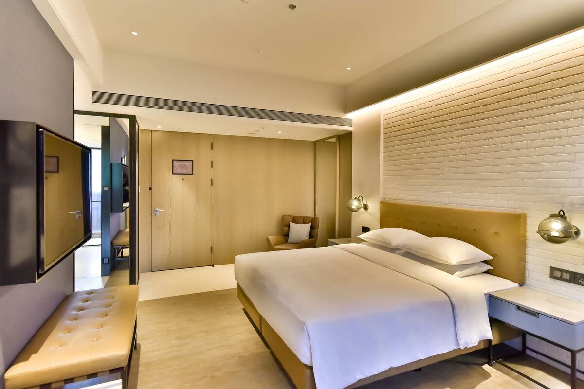 A modern hotel room with a large bed, a bedside table, a bench, a TV, and a wardrobe.