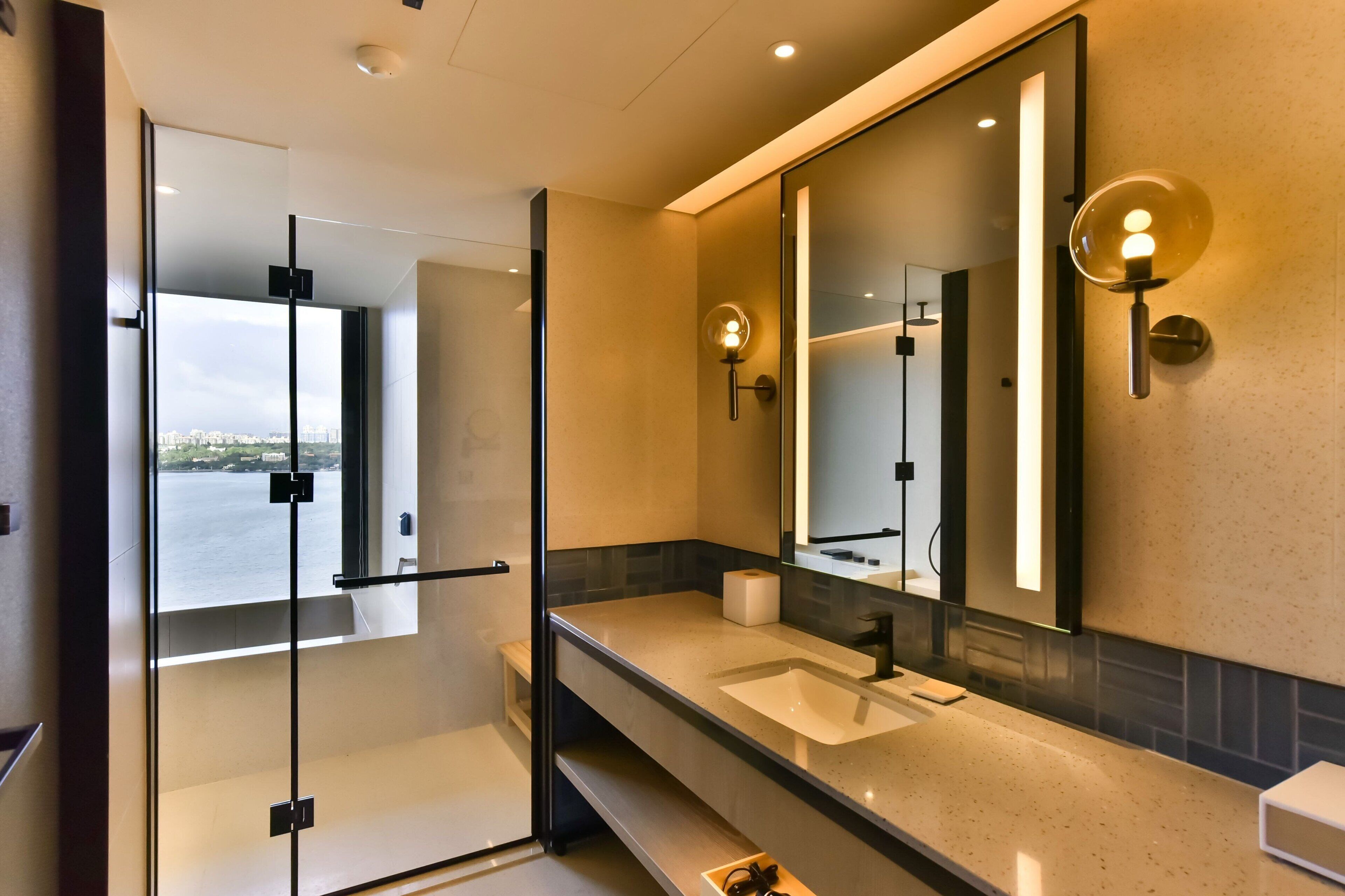 A modern bathroom with a large mirror, a sink, and a glass shower enclosure.