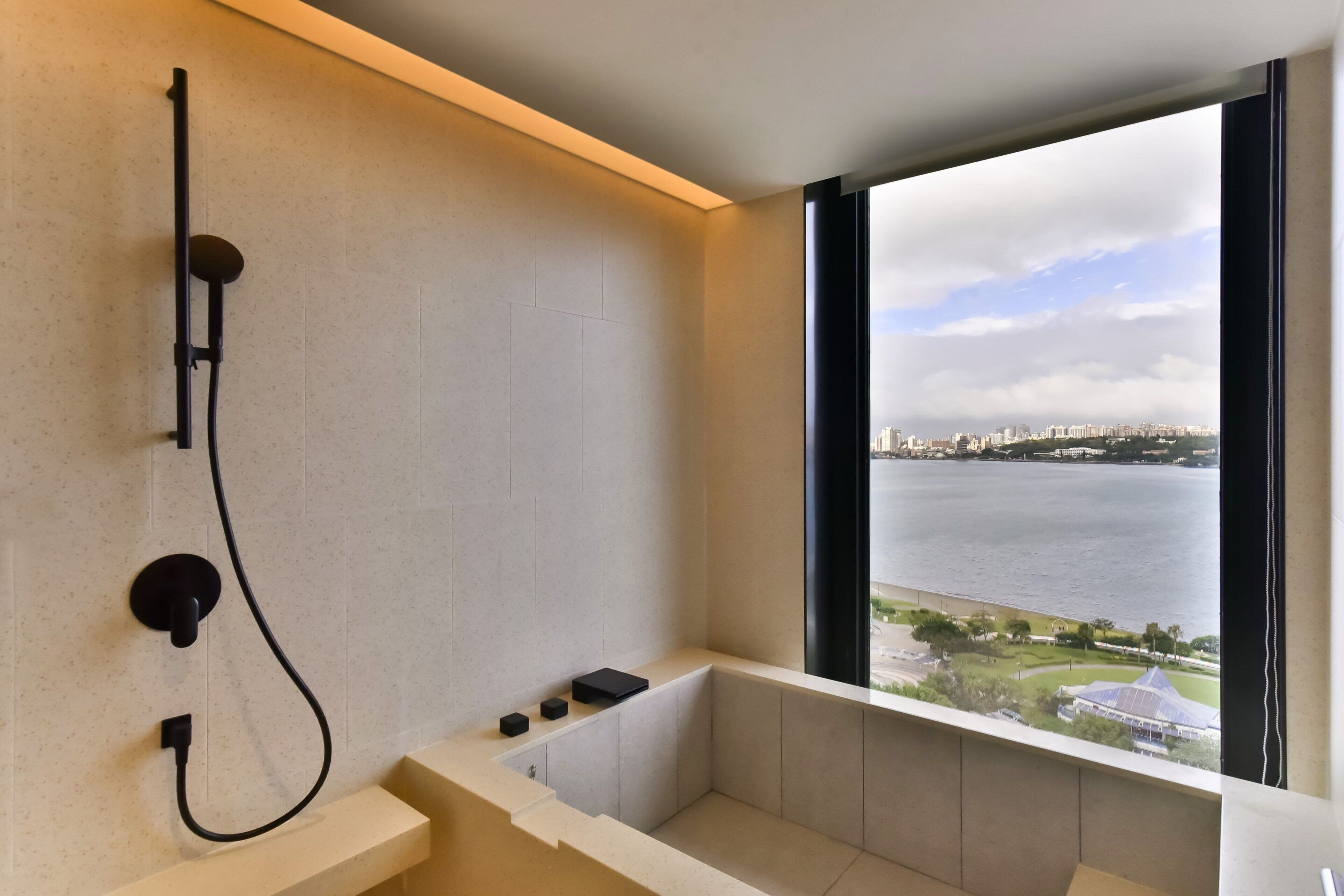 A modern bathroom with a bathtub, a showerhead, and a view of a cityscape through a large window.