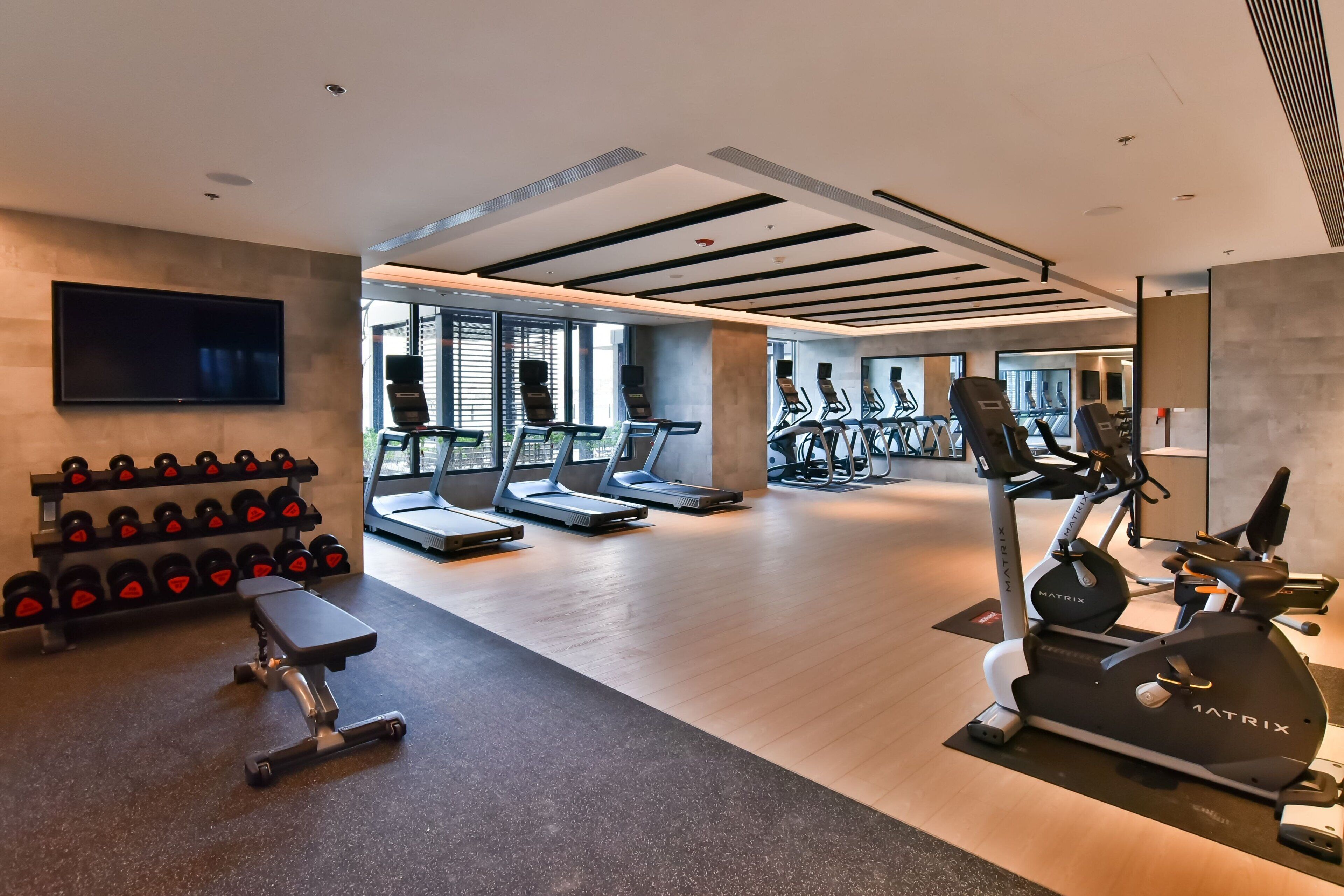Ein modernes Fitnessstudio mit Laufbändern, Crosstrainern, Kurzhanteln und einer Trainingsbank.