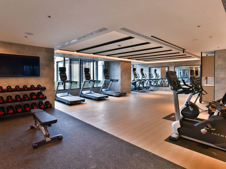Ein modernes Fitnessstudio mit Laufbändern, Crosstrainern, Kurzhanteln und einer Trainingsbank.