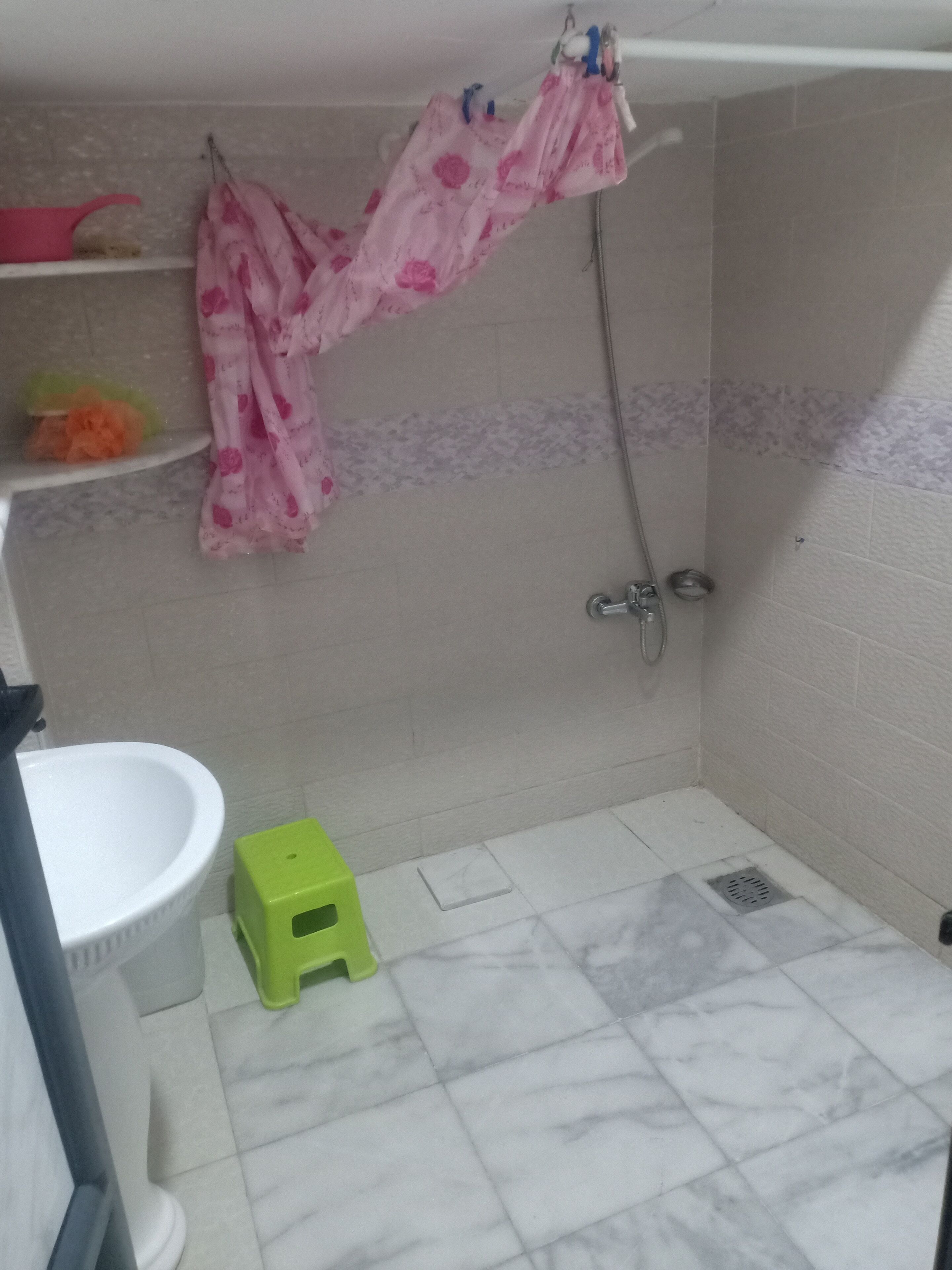 Een badkamer met een douche, toilet, wastafel en een klein krukje.