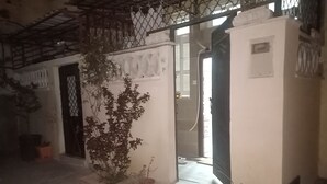 A building entrance with a metal gate, a potted plant, and a concrete pathway leading to a door. - Dream Home (Setif)
