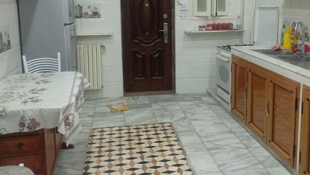 A compact kitchen with a wooden door, white cabinets, a tiled floor, and a dining area with a table and chairs. - Dream Home (Setif)