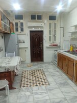 A compact kitchen with a wooden door, white cabinets, a tiled floor, and a dining area with a table and chairs.