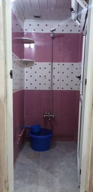 A small bathroom with pink and white tiled walls, a shower, and two blue buckets.