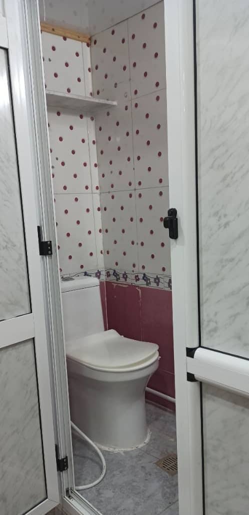 A bathroom with a toilet, a shower area, and a tiled wall with a polka dot pattern.