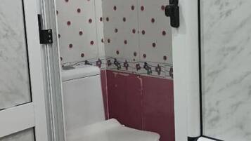 A bathroom with a toilet, a shower area, and a tiled wall with a polka dot pattern.