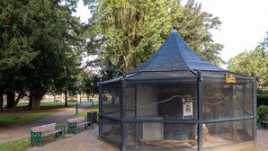 Un kiosque doté d’un toit bleu et d’une enceinte en treillis, entouré de bancs et d’arbres.