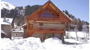 Eine zweistöckige Holzchalet mit Balkon, umgeben von Schnee und Bergen.