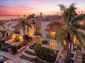 A coastal residential area with houses featuring balconies, outdoor seating, and a view of the ocean at sunset.
