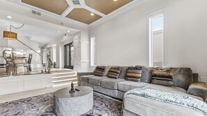 A spacious living room with a grey sofa, patterned rug, and a round coffee table. - Windansea Luxury Beach Home  - Spa, AC, Walk to Beach, Garage & Fast WiFi! (La Jolla)