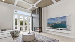 A modern living room with a fireplace, a large TV, and a view of San Diego. - Windansea Luxury Beach Home  - Spa, AC, Walk to Beach, Garage & Fast WiFi! (La Jolla)