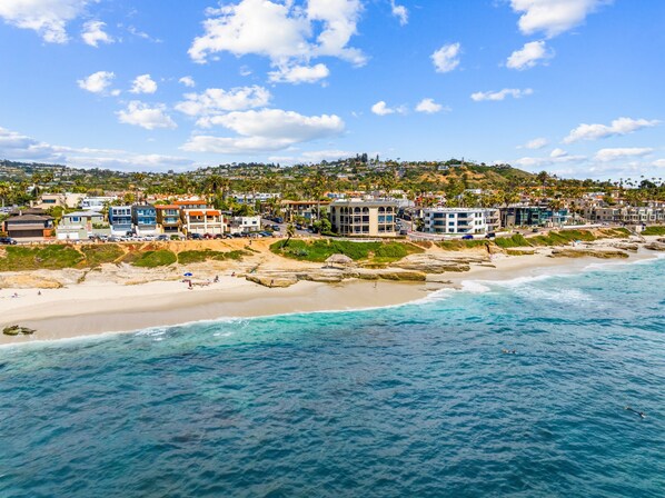 A coastal town with beachfront properties, clear blue skies, and rocky shoreline.