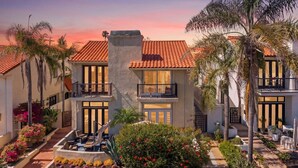 A two-story building with a red-tiled roof, balconies, and a landscaped garden with various plants and flowers. - Windansea Luxury Beach Home  - Spa, AC, Walk to Beach, Garage & Fast WiFi! (La Jolla)