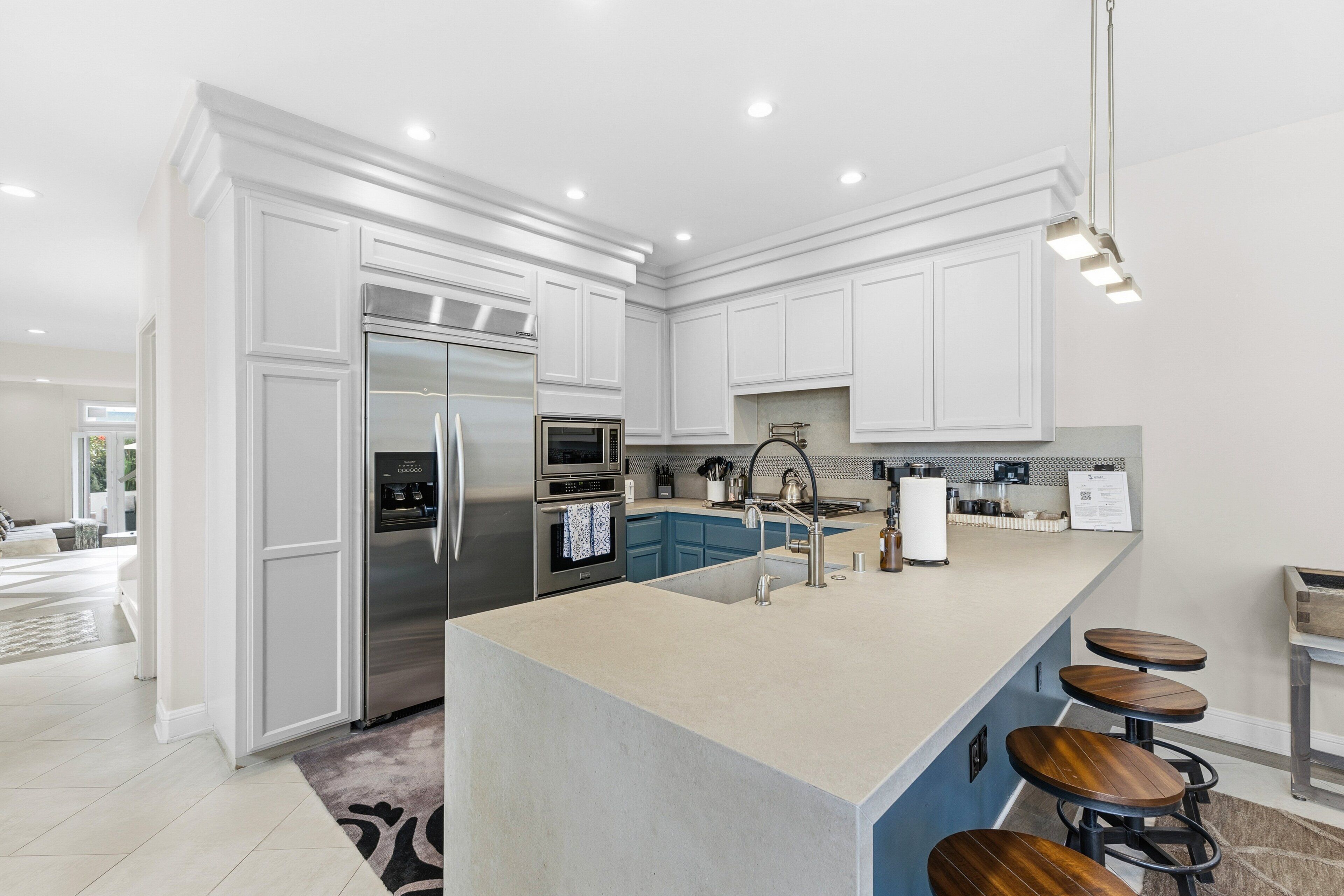 A modern kitchen with white cabinetry, stainless steel appliances, a large island with stools, and recessed lighting.