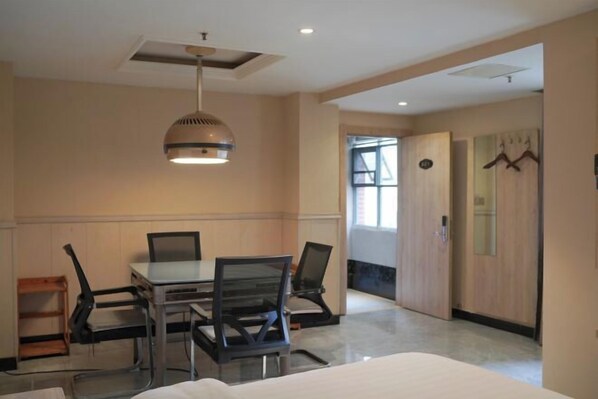 A hotel room with a bed, a desk with chairs, a hanging lamp, a door, and a window. - Xingelin Business Hotel (Daye)