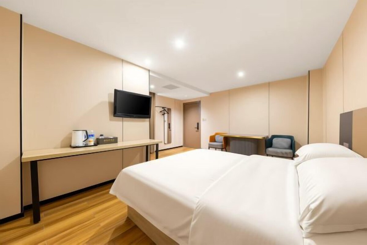 Habitación de hotel con cama, escritorio, televisor y zona de ducha.