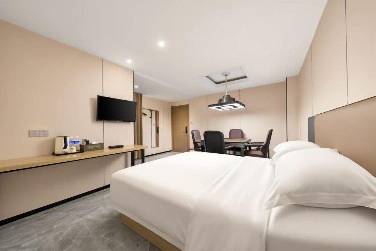 Habitación de hotel con cama, escritorio con silla, televisor de pantalla plana montado en la pared y lámpara en el techo.