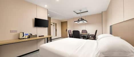 A hotel room with a bed, a desk with a chair, a flat-screen TV mounted on the wall, and a ceiling light fixture.
