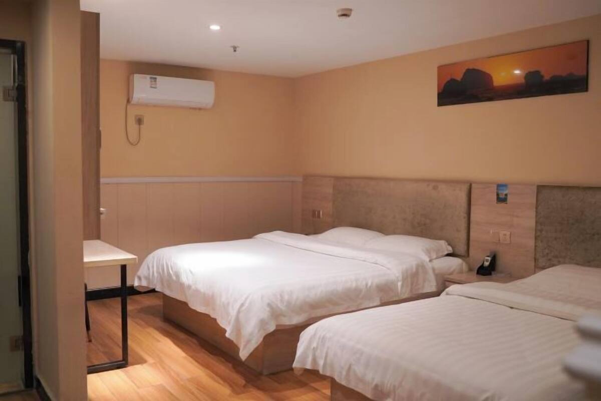 A hotel room with two beds, a desk, an air conditioning unit, and a painting on the wall.