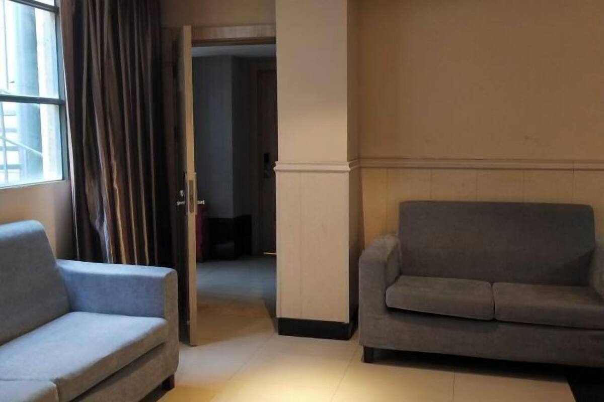 A room with two sofas, a window with curtains, and a door leading to another room.