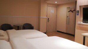 A hotel room with two beds, a small table, two chairs, a television, and a door with a sign.
