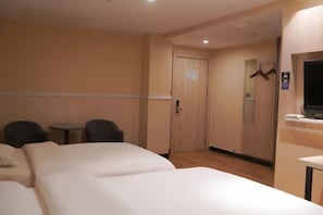 Habitación de hotel con dos camas, una mesita, dos sillas, un televisor y una puerta con un cartel.