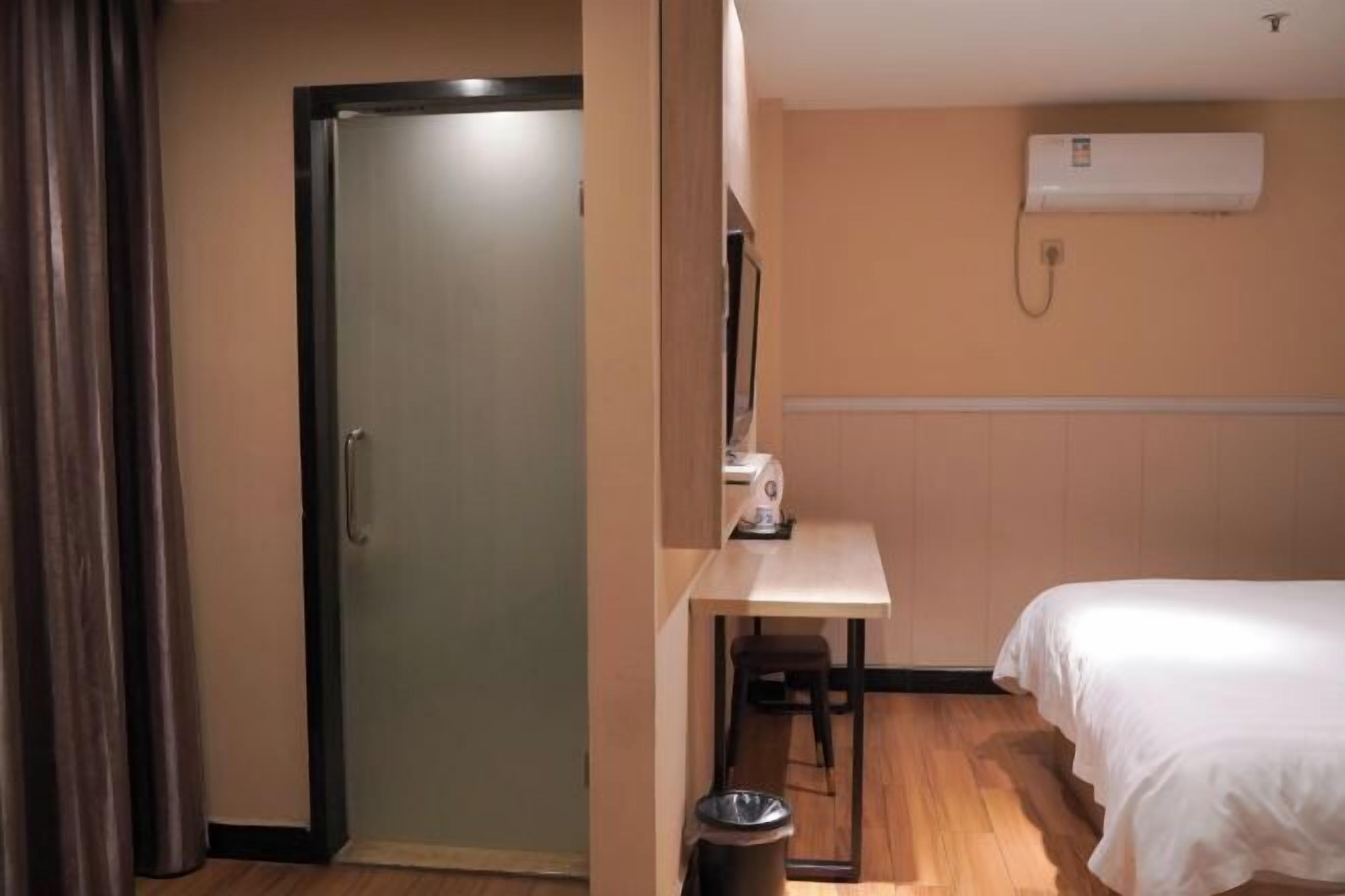 Quarto de hotel com cama, escrivaninha, cadeira, lixeira e aparelho de ar condicionado.