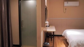 Habitación de hotel con cama, escritorio, silla, basurero y unidad de aire acondicionado.