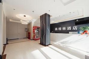 Zona de recepción de un hotel con diseño moderno, que incluye un mostrador de recepción, una máquina expendedora y un pilar grande.
