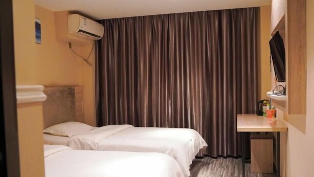 Una habitación de hotel con dos camas, una mesita, un televisor y una cortina.