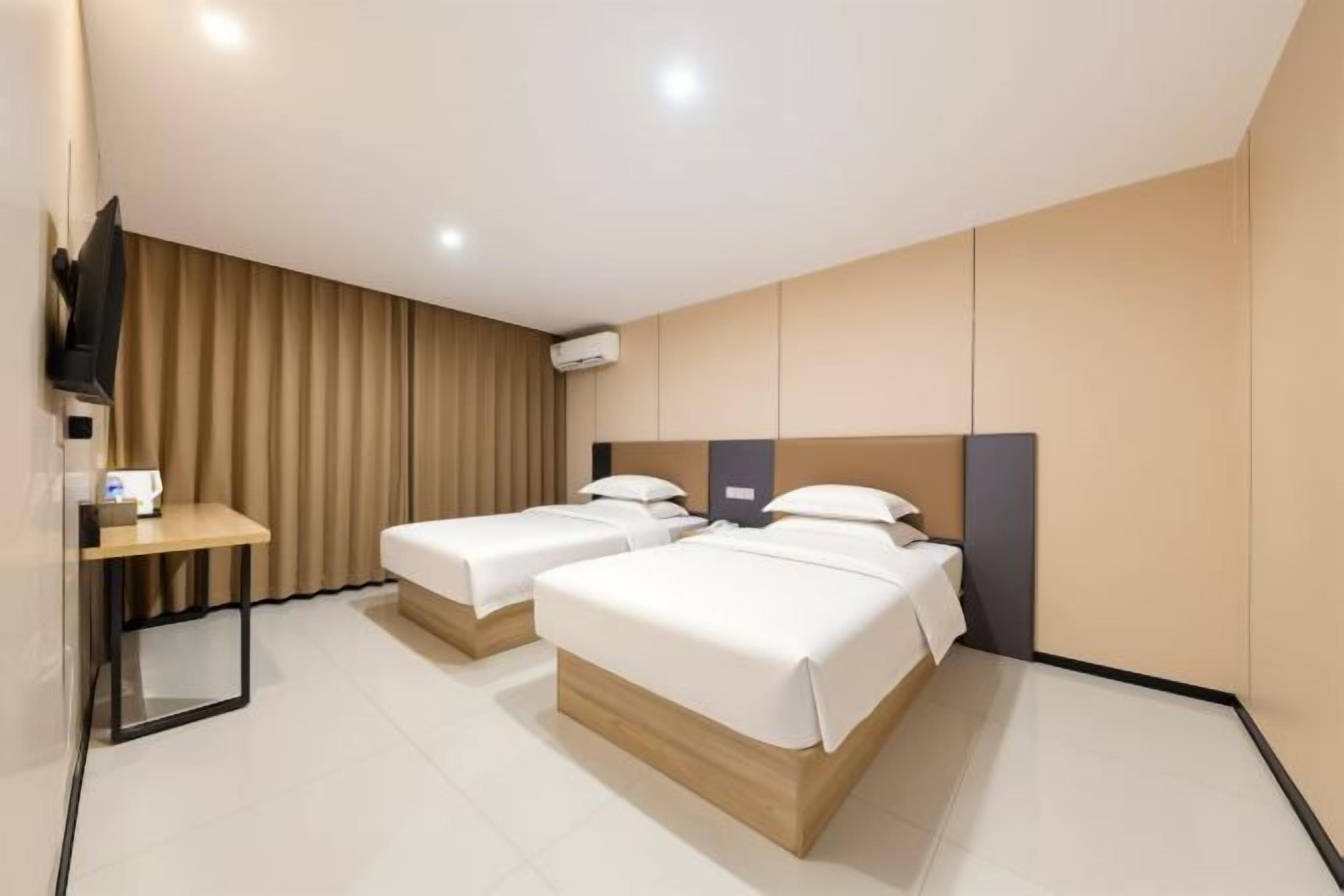 A hotel room with two beds, a desk, and a TV.