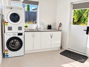 Cocina compacta con lavadora y secadora integradas, un lavamanos, armarios y una puerta con vistas a zonas verdes.