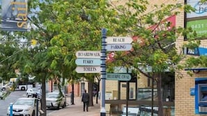 En vägvisare med flera pilar som pekar åt olika håll och visar vägen till olika faciliteter, till exempel strand, parkering, strandpromenad, färja, toaletter och en hjälplinje.
