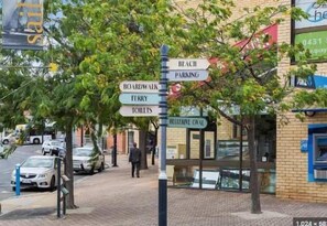 A directional signpost with multiple arrows pointing to various amenities such as beach, parking, boardwalk, ferry, toilets, and a helpline.