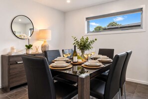 A dining area with a glass table, black chairs, and a view of the sky through a window.