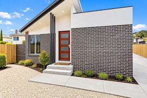 A modern house with a brick exterior, a wooden door, and a small front garden.