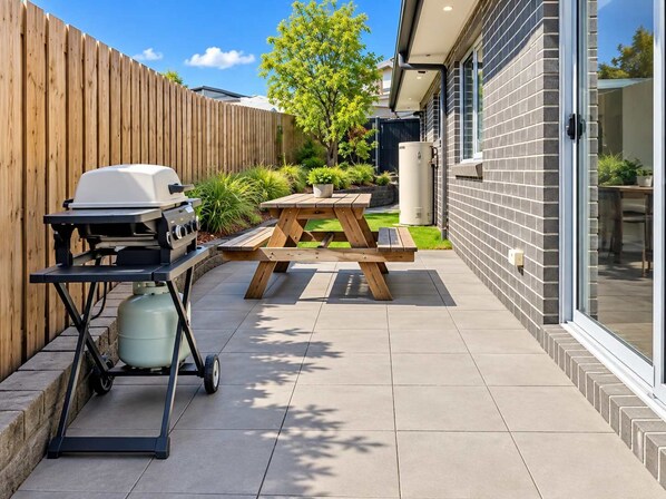 A patio with a barbecue grill, a picnic table, and a water tank.